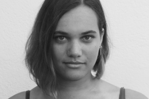 Black and white headshot of a young woman with an asymmetrical bob. She has brown skin and a serious expression.