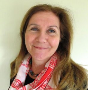 A woman wearing a red and white scarf smiles at the camera. She has long brown hair.
