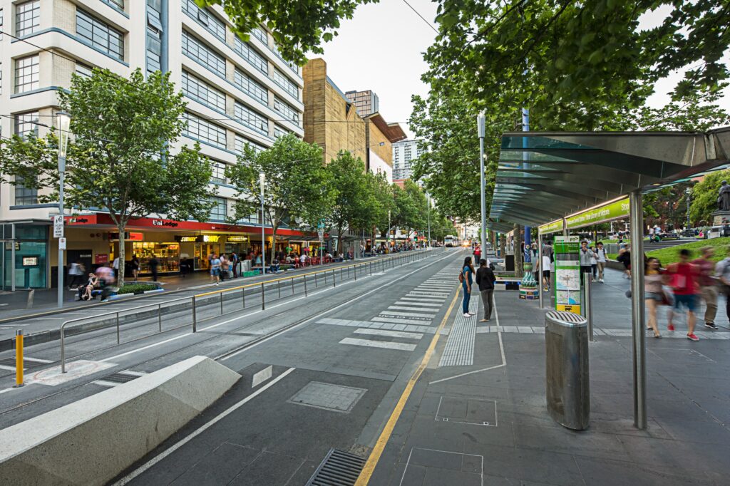 A tram stop in Melbourne, with buildings on the left side of the road and a tram stop shelter on the right.